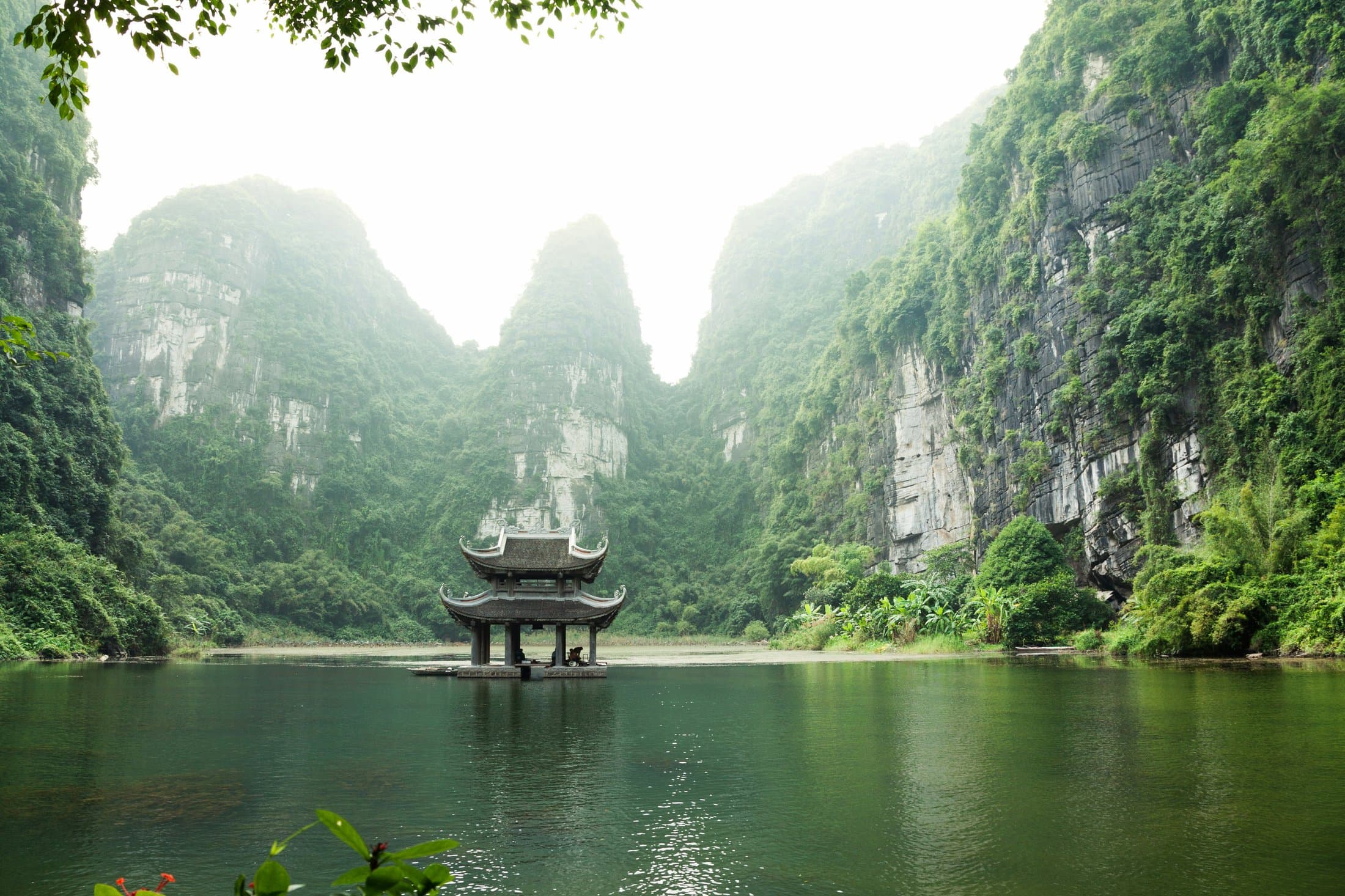 Cảnh núi đá vôi Việt Nam trong sương với kiến trúc truyền thống phản chiếu trên mặt nước.